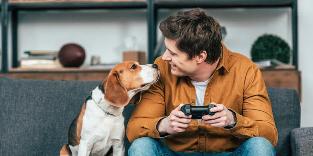 Un homme assis sur son canapé avec son chien qui joue aux jeux vidéos